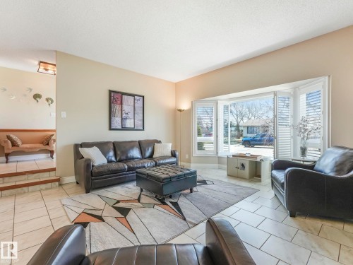 Bright living area featuring a large bay window with plantation shutters, light-toned tile flooring, and neutral wall paint - 1027 77 Street, Edmonton, AB - Indoor Photo Showing Living Room