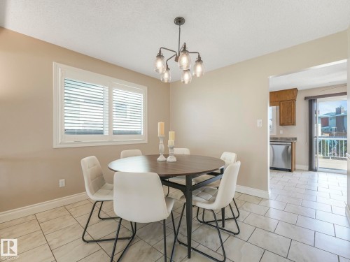 Dining area with a contemporary chandelier, large window with white louvered blinds, and light-toned tile flooring - 1027 77 Street, Edmonton, AB - Indoor Photo Showing Dining Room