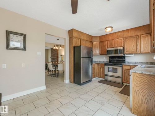 Kitchen featuring stainless steel appliances, wood cabinetry, light-toned countertops, and tile flooring - 1027 77 Street, Edmonton, AB - Indoor Photo Showing Kitchen With Double Sink
