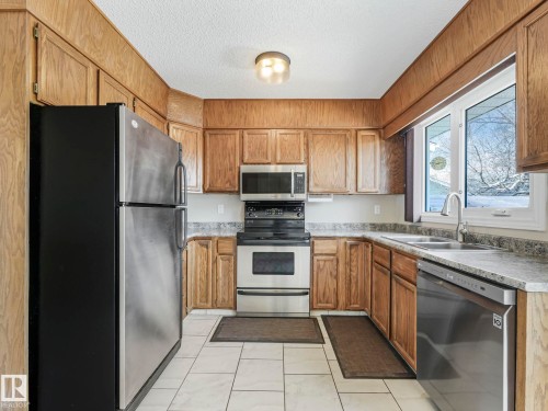Kitchen featuring light wood cabinetry, stainless steel appliances, speckled countertops, and white tile flooring - 1027 77 Street, Edmonton, AB - Indoor Photo Showing Kitchen With Double Sink