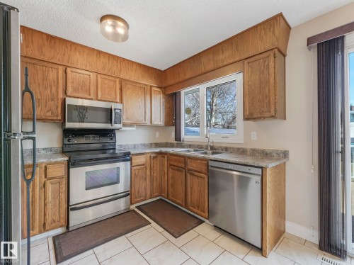 Kitchen featuring oak cabinetry, light-toned countertops, and stainless steel appliances including a range, microwave, and dishwasher - 1027 77 Street, Edmonton, AB - Indoor Photo Showing Kitchen With Double Sink