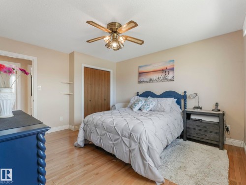 Bright bedroom featuring wood-finish flooring, a brass-toned ceiling fan with integrated lighting, and a double-door closet with wood-finish panels - 1027 77 Street, Edmonton, AB - Indoor Photo Showing Bedroom