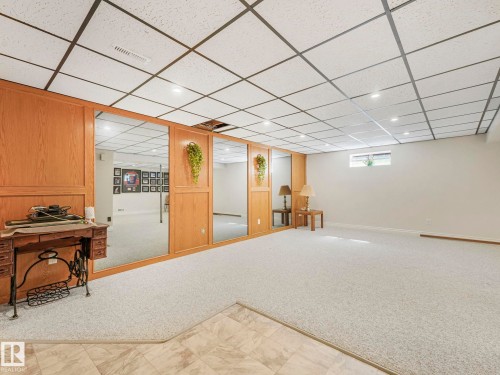 Finished basement space featuring a drop ceiling with recessed lighting, light-toned carpeting, and a wood-paneled wall with integrated mirrors - 1027 77 Street, Edmonton, AB - Indoor