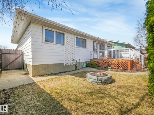 Expansive backyard featuring a stone fire pit, a concrete patio, and a wood deck with white railings - 1027 77 Street, Edmonton, AB - Outdoor With Deck Patio Veranda With Exterior