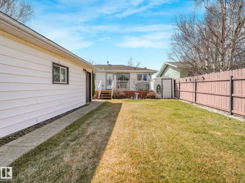 Spacious backyard featuring a manicured lawn, a detached garage with white siding, and a rear deck with white railings - 1027 77 Street, Edmonton, AB - Outdoor