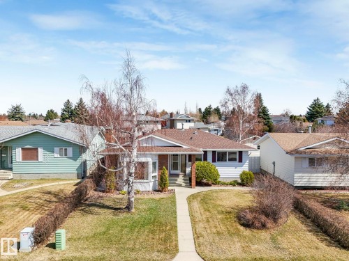 Ranch-style exterior with white siding, a brown shingle roof, and a mature front yard tree - 1027 77 Street, Edmonton, AB - Outdoor With Facade