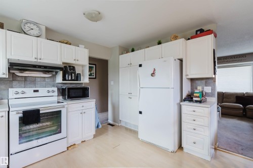 Kitchen featuring white cabinetry, tile backsplash, white appliances, and wood-finish flooring - 10519 36A Avenue, Edmonton, AB - Indoor Photo Showing Kitchen