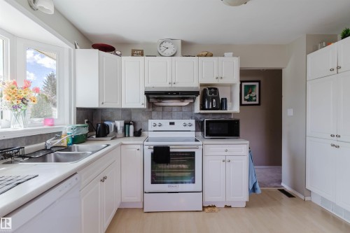 White cabinetry and light wood-finish flooring define this kitchen - 10519 36A Avenue, Edmonton, AB - Indoor Photo Showing Kitchen With Double Sink
