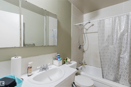 Bathroom featuring a vanity with an integrated sink, a three-panel mirrored medicine cabinet, and a white tiled shower/tub combination with a shower head and handheld spray - 10519 36A Avenue, Edmonton, AB - Indoor Photo Showing Bathroom