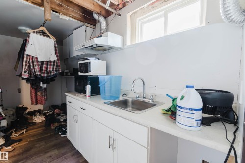 Utility area featuring a stainless steel sink with chrome faucet, white base cabinetry, and wood-finish flooring - 10519 36A Avenue, Edmonton, AB - Indoor