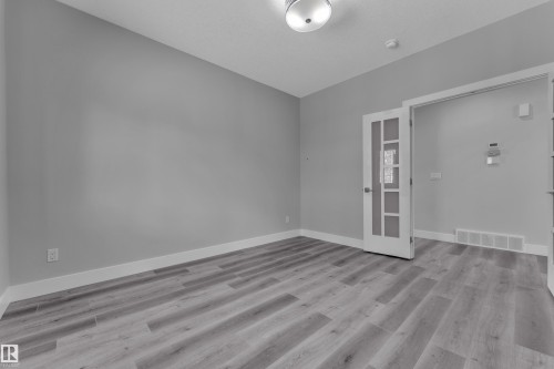 Room featuring wood-finish flooring, light grey walls, white baseboards, and a glass-paneled interior door - 4403 Triomphe Gate, Beaumont, AB - Indoor Photo Showing Other Room
