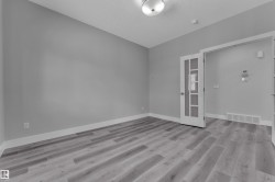 Room featuring wood-finish flooring, light grey walls, white baseboards, and a glass-paneled interior door - 