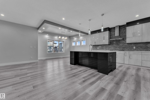 Open-concept kitchen featuring a dark grey brick-style backsplash, stainless steel range hood, and light-tone wood-finish flooring - 4403 Triomphe Gate, Beaumont, AB - Indoor Photo Showing Kitchen With Upgraded Kitchen
