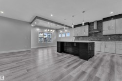 Open-concept kitchen featuring a dark grey brick-style backsplash, stainless steel range hood, and light-tone wood-finish flooring - 