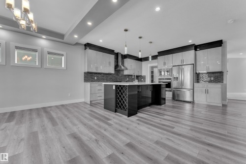 Open-concept kitchen featuring an island with integrated wine storage, stainless steel appliances, a mosaic tile backsplash, wood-finish flooring, and recessed ceiling lighting - 4403 Triomphe Gate, Beaumont, AB - Indoor Photo Showing Kitchen With Upgraded Kitchen