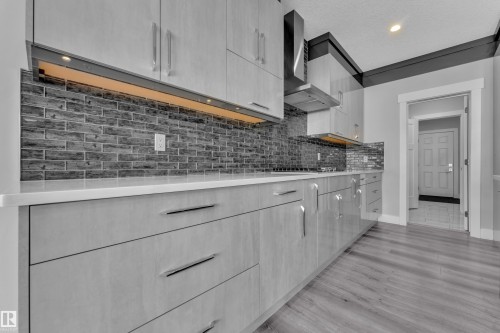 Contemporary kitchen featuring light wood-finish cabinetry, solid surface countertops, and a dark tile backsplash - 4403 Triomphe Gate, Beaumont, AB - Indoor Photo Showing Kitchen