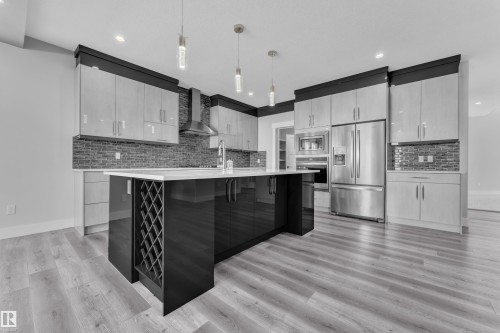 Kitchen featuring a central island with integrated wine storage, stainless steel appliances, light wood-finish flooring, a mosaic tile backsplash, and contemporary pendant lighting - 4403 Triomphe Gate, Beaumont, AB - Indoor Photo Showing Kitchen With Upgraded Kitchen