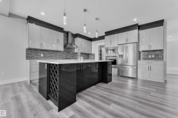 Kitchen featuring a central island with integrated wine storage, stainless steel appliances, light wood-finish flooring, a mosaic tile backsplash, and contemporary pendant lighting - 