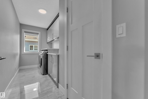 Dedicated laundry room featuring large format tile flooring, a window providing natural light, built-in cabinetry with under-cabinet lighting, and a countertop workspace - 4403 Triomphe Gate, Beaumont, AB - Indoor