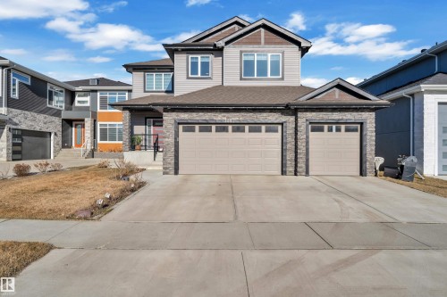 Contemporary two-story residence featuring a two-car garage with individual doors, stone facade accents, light gray siding, and a prominent front entry with a black railing - 4403 Triomphe Gate, Beaumont, AB - Outdoor With Facade