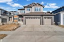 Contemporary two-story residence featuring a two-car garage with individual doors, stone facade accents, light gray siding, and a prominent front entry with a black railing - 4403 Triomphe Gate, Beaumont, AB  - Outdoor With Facade 