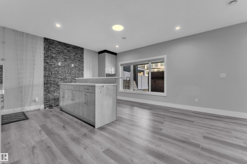 Open-concept room featuring light wood-finish flooring, a stone-accented wall, and recessed lighting - 4403 Triomphe Gate, Beaumont, AB - Indoor