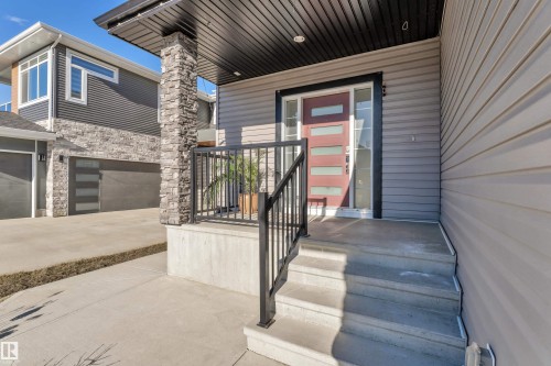 Contemporary exterior featuring light gray siding, a prominent stone-clad column, and a modern entryway with a red door - 4403 Triomphe Gate, Beaumont, AB - Outdoor With Exterior