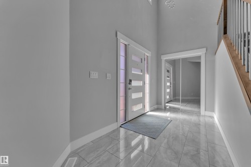 Entryway featuring a contemporary front door with frosted glass panels, large format tile flooring, a mirrored closet, and a staircase with wood treads and metal balusters - 4403 Triomphe Gate, Beaumont, AB - Indoor Photo Showing Other Room