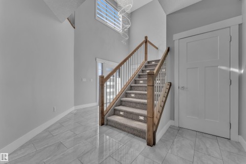 Two-story foyer featuring a grand staircase with wood newel posts, white balusters, and carpeted treads with integrated lighting - 4403 Triomphe Gate, Beaumont, AB - Indoor Photo Showing Other Room