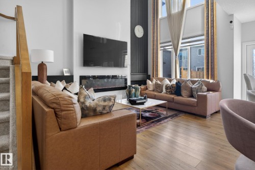 Spacious living area featuring wood-finish flooring, a linear electric fireplace, and a tall accent wall with vertical paneling - 3605 42 Avenue, Beaumont, AB - Indoor Photo Showing Living Room With Fireplace