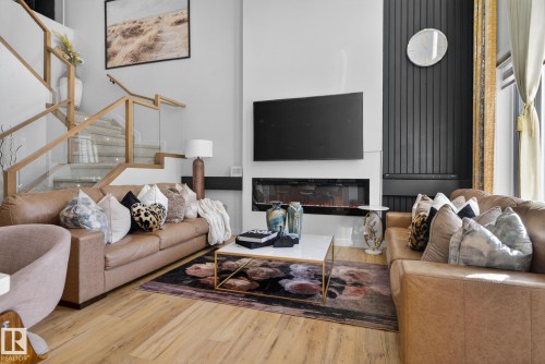 Living area featuring a modern linear fireplace, a wall-mounted display, and light wood-finish flooring - 3605 42 Avenue, Beaumont, AB - Indoor Photo Showing Living Room With Fireplace