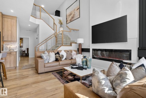 Open-concept living area with wood-finish flooring, a contemporary fireplace, and a light wood staircase featuring clear panel railings - 3605 42 Avenue, Beaumont, AB - Indoor Photo Showing Living Room With Fireplace