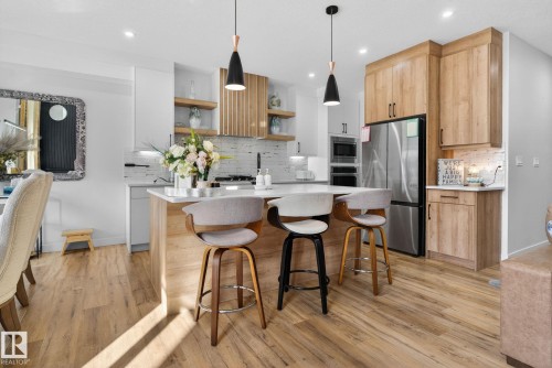 Kitchen featuring a large central island with seating, stainless steel appliances, wood-finish flooring, recessed lighting, and a white tile backsplash - 3605 42 Avenue, Beaumont, AB - Indoor Photo Showing Kitchen With Stainless Steel Kitchen With Upgraded Kitchen