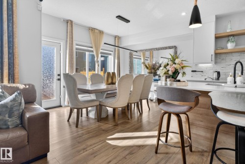 Open-concept dining area featuring wood-finish flooring, a contemporary linear chandelier, and a frosted glass-paneled exterior door - 3605 42 Avenue, Beaumont, AB - Indoor Photo Showing Dining Room