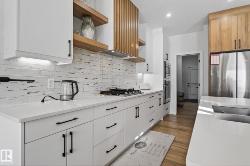Modern kitchen featuring white cabinetry with black hardware, white countertops, a tiled backsplash, wood-finish flooring, and stainless steel appliances - 3605 42 Avenue, Beaumont, AB - Indoor Photo Showing Kitchen With Upgraded Kitchen