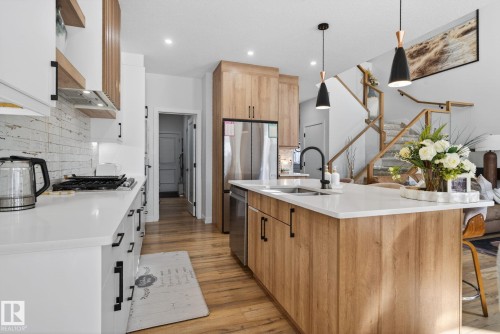 Contemporary kitchen featuring a large central island with a sink and pendant lighting, stainless steel appliances, wood-finish flooring, and a white subway tile backsplash - 3605 42 Avenue, Beaumont, AB - Indoor Photo Showing Kitchen With Double Sink With Upgraded Kitchen
