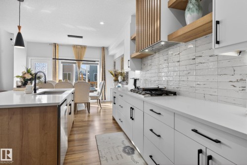 Modern kitchen featuring white cabinetry with matte black hardware, quartz countertops, a gas cooktop, and a textured white subway tile backsplash - 3605 42 Avenue, Beaumont, AB - Indoor Photo Showing Kitchen With Upgraded Kitchen