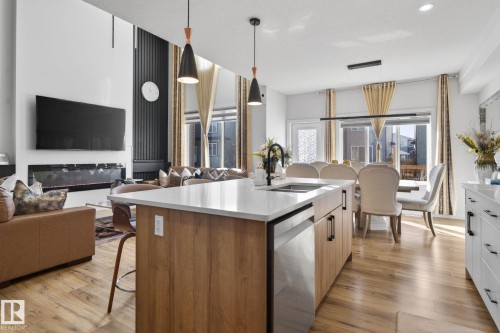 Open-concept living area featuring a kitchen island with quartz countertops, wood-finish flooring, a linear electric fireplace, and a dining area with pendant lighting - 3605 42 Avenue, Beaumont, AB - Indoor Photo Showing Kitchen With Double Sink With Upgraded Kitchen