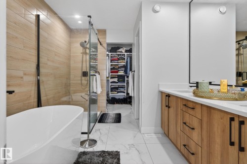 Contemporary bathroom featuring a freestanding tub, glass-enclosed shower with wood-finish tile surround, and a dual vanity with white countertops and wood-finish cabinetry - 3605 42 Avenue, Beaumont, AB - Indoor Photo Showing Bathroom