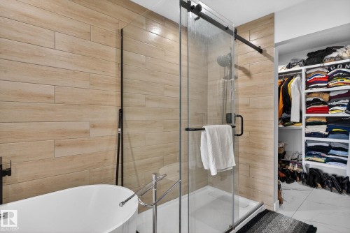Modern bathroom featuring a freestanding soaking tub, a glass-enclosed shower with matte black hardware, and wood-finish tile wall - 3605 42 Avenue, Beaumont, AB - Indoor Photo Showing Bathroom