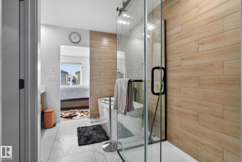Contemporary bathroom featuring a spacious glass-enclosed shower with black trim, wood-finish tiled shower wall, and white marble-look floor tiles - 3605 42 Avenue, Beaumont, AB - Indoor Photo Showing Bathroom