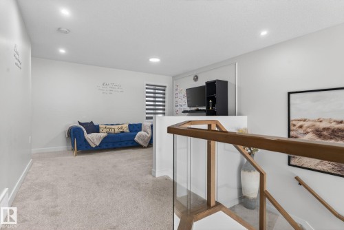 Carpeted upper-level landing featuring recessed lighting, a modern glass and wood banister, and a window with horizontal blinds - 3605 42 Avenue, Beaumont, AB - Indoor Photo Showing Other Room