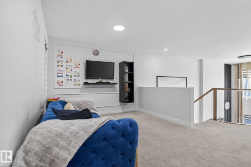 Carpeted loft area featuring a modern wall-mounted entertainment unit, recessed lighting, and a contemporary glass and wood-finish railing system - 3605 42 Avenue, Beaumont, AB - Indoor Photo Showing Bedroom