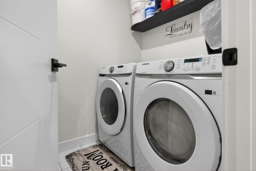 Dedicated laundry area featuring modern white appliances, a dark floating shelf for storage, and white trim - 3605 42 Avenue, Beaumont, AB - Indoor Photo Showing Laundry Room