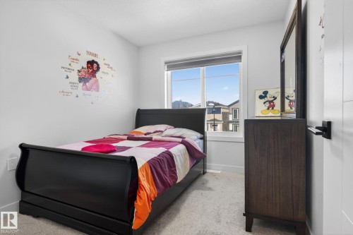 Carpeted room featuring a large window, white trim, and a dark wood dresser with an attached mirror - 3605 42 Avenue, Beaumont, AB - Indoor Photo Showing Bedroom