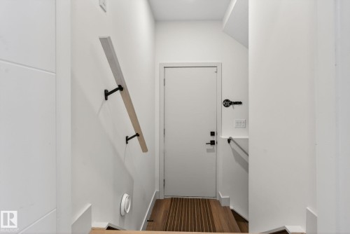 Hardwood flooring leading to a white door with black hardware, complemented by a light-toned wood handrail with black brackets - 3605 42 Avenue, Beaumont, AB - Indoor Photo Showing Other Room