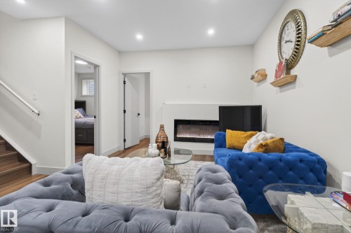 Living area featuring a modern linear electric fireplace, wood-finish flooring, recessed lighting, and a partial staircase with a white handrail - 3605 42 Avenue, Beaumont, AB - Indoor With Fireplace