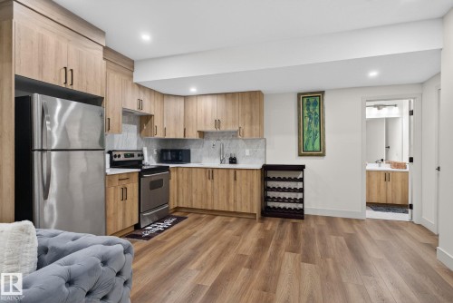 Compact kitchen featuring wood-finish cabinetry, stainless steel appliances, and a light-toned countertop with a stone-look backsplash - 3605 42 Avenue, Beaumont, AB - Indoor Photo Showing Kitchen With Stainless Steel Kitchen