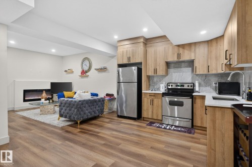Open concept living area featuring wood-finish flooring, a contemporary kitchen, and a built-in electric fireplace - 3605 42 Avenue, Beaumont, AB - Indoor Photo Showing Kitchen