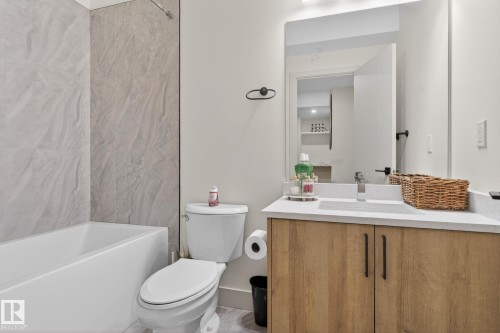 Bathroom featuring a full-size bathtub with surrounding tile, a modern vanity with wood-finish cabinetry, a large mirror, and a recessed sink with a single-handle faucet - 3605 42 Avenue, Beaumont, AB - Indoor Photo Showing Bathroom